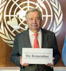 Man holding #weremember sign next to Unesco flag